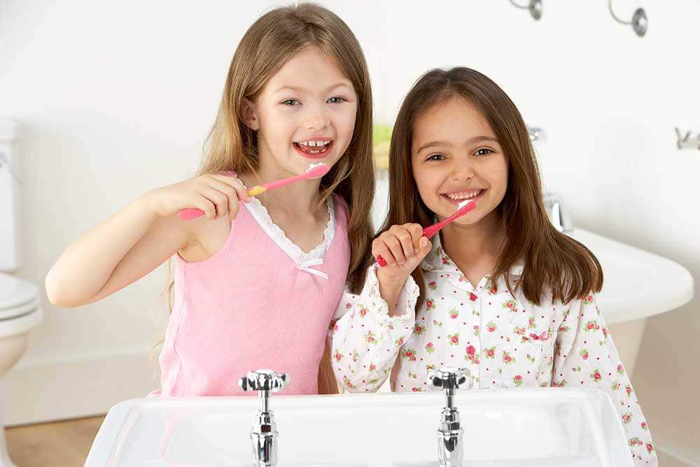 Two smiling children brushing their teeth.