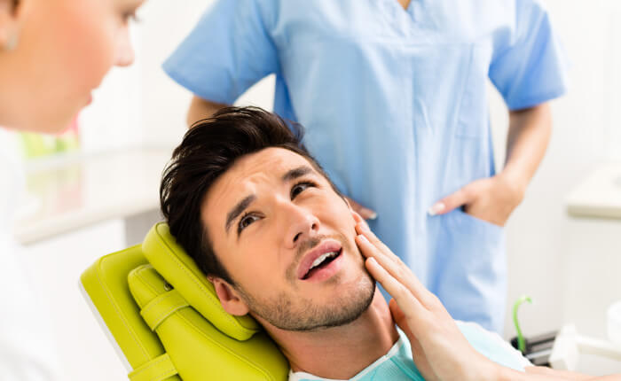 man at emergency dental appointment holding mouth