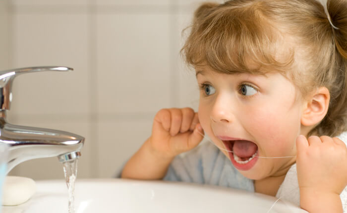 young girl flossing teeth in front of sink