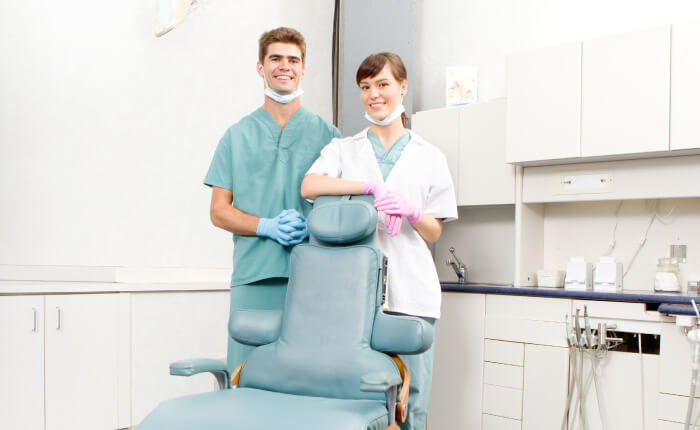 periodontist and dental assistant in treatment room leaning on dental chair
