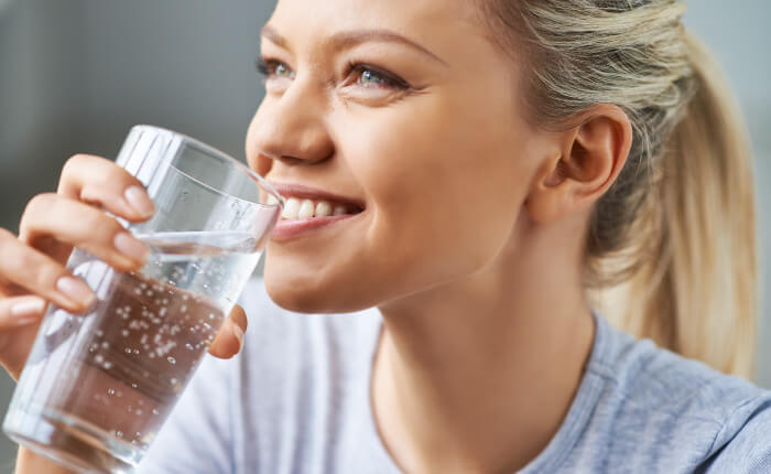 Woman with blonde hair smiling as she drinks water