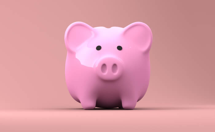 Frontal view of pink piggy bank that holds money in front of a darker pink backdrop