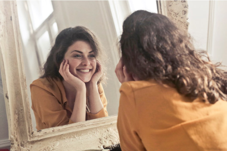 girl smiling into a mirror after teeth whitening treatments