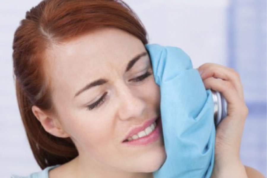 woman holds an ice pack to her jaw after oral surgery
