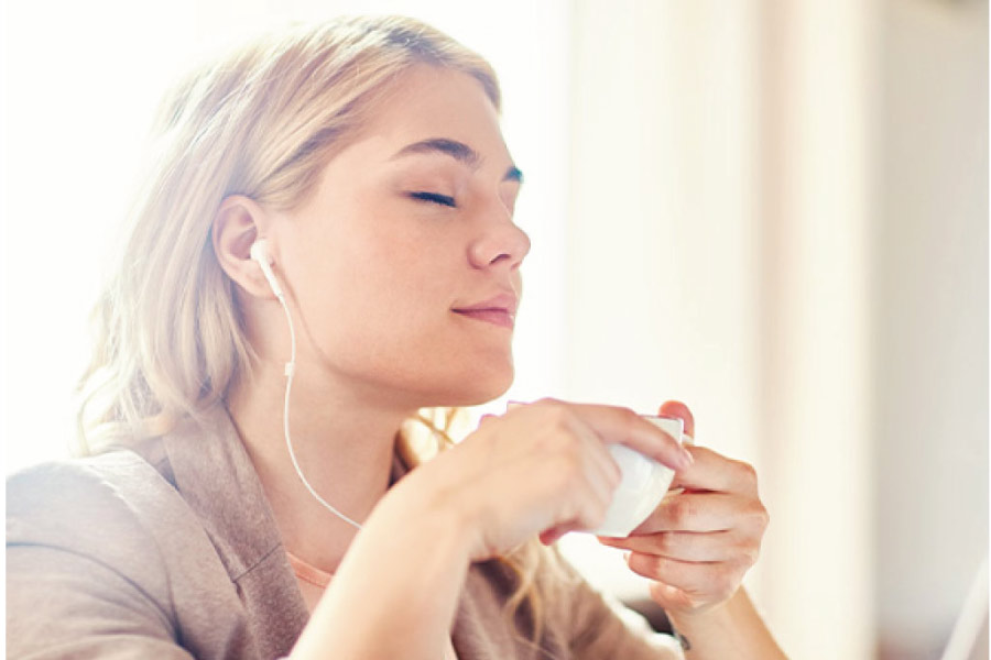 woman relaxes with earphones and a calming beverage before visiting the dentist